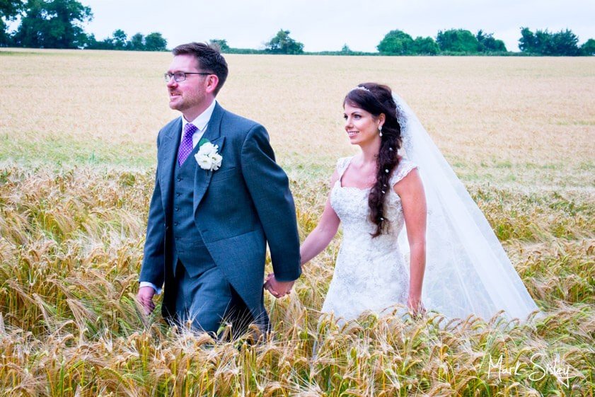 Bride and Groom walking through wheat field - wedding at Clearwell Castle - Mark Sisley Photography