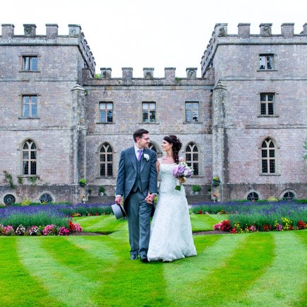 Bride and groom walking in front of lavender hedge at Clearwell Castle on their wedding day