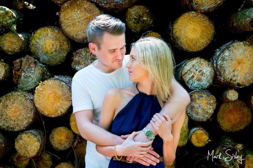 rustic portrait of man and woman in front of logs - family portrait photograph - Mark Sisley Photography