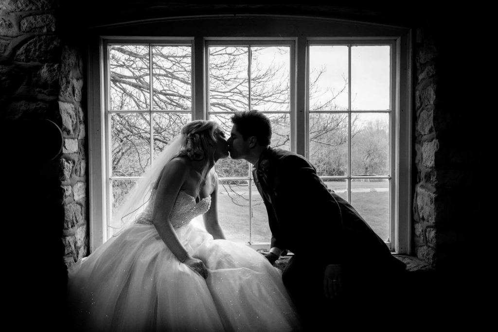 Notley Tythe Barn wedding photography - silhouette image of bride and groom kissing in the window