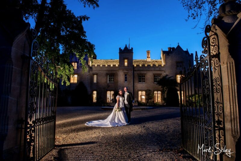 Floodlit night pose of the bride and groom under dusky blue skies on the long driveway outside the entrance to their Oxfordshire wedding venue