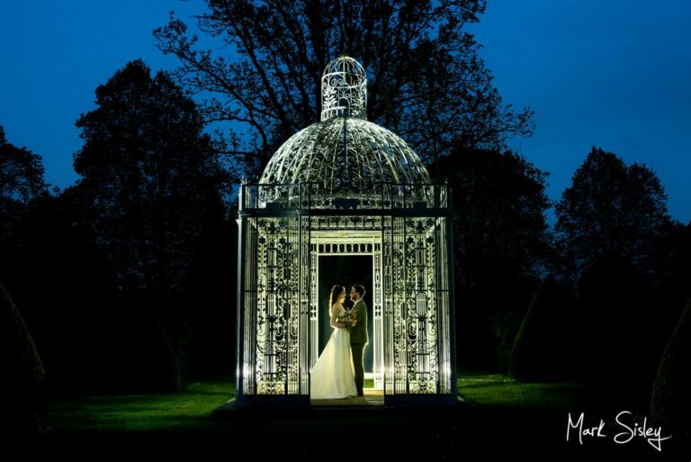 The newlyweds dramatically captured in silhouette at night-time under the wrought iron Birdcage Pergola at their Chenies Manor wedding