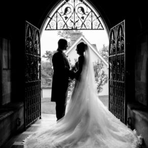 Black and white wedding photography in Buckinghamshire - silhouette image of bride and groom in arched doorway at their church