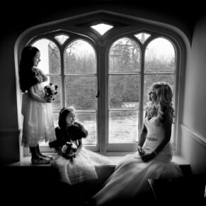 Black and white wedding photography in Buckinghamshire - silhouette image of bride and flower girls in arched window at Taplow House Hotel