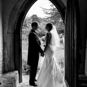 Black and white full length silhouette portrait of bride and groom in arched doorway at Nether Winchendon church wedding