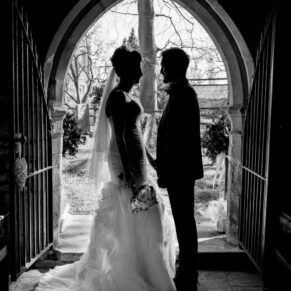 Black and white wedding photography in Buckinghamshire - Silhouette image of bride and groom as they leave the chapel at their Dorton House ceremony
