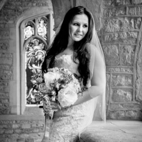 Black and white wedding photography in Buckinghamshire - bride in front of stained glass window in stunning church