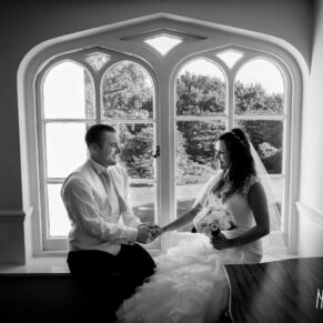 Black and white portrait of bride and groom framed by dramatic arched window at Taplow House Hotel wedding