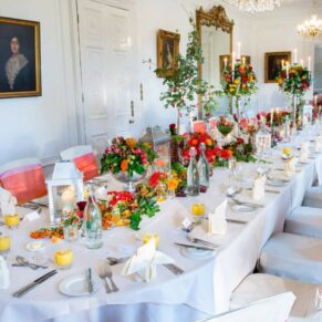 Taplow House hotel wedding breakfast laid out with autumnal centerpiece of ivy, orange and red berries, chestnuts and eucalyptus, with white chair covers and pink and orange sashes