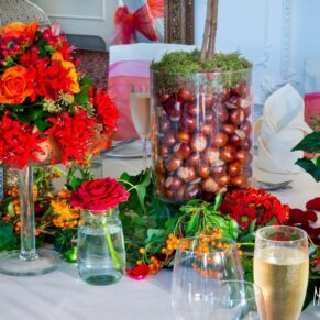 Autumnal wedding breakfast place setting with chestnuts, yellow and red berries, and orange and red roses in jars and ivy