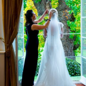 Bridemaid fixing veil for bride in full length window at Taplow House Hotel wedding