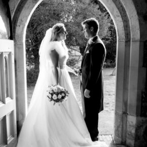 Black and white portrait of bride and groom in doorway of church at Hampden House winter wedding