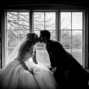 Black and white portrait of bride and groom in window silhouette at Notley Tythe Barn winter wedding