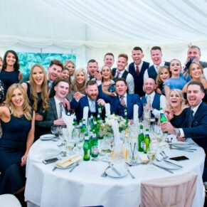 Summer's day group pose of lots of wedding guests inside the marquee at Missenden Abbey