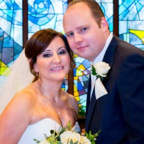 The newlyweds pose by the stained glass window at their St Josephs Church wedding in Thame