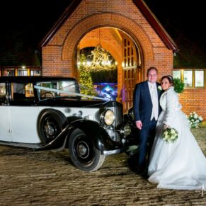 Waddesdon Dairy Christmas wedding pose with the car at the entrance after dusk