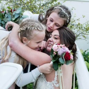 The bridesmaids give a huge embracing hug to the bride at the front of the historic venue