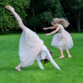 Cartwheel photography capture of two smiling wedding flower girls enjoying the moment in the lovely gardens of Sopwell House Hotel
