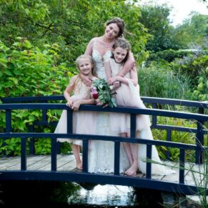 The happy bride gives her two gorgeous flower girls a big hug on the bridge