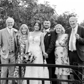 Photography of the newlyweds with their parents in a relaxed pose on the bridge at their Sopwell House wedding