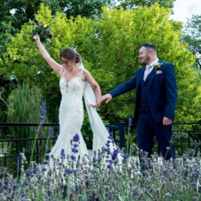 Photography of the smiling bride as she punches the air as she strolls through the gardens with her husband at their Sopwell House Hotel wedding reception