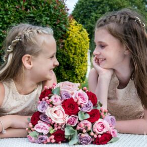 Two young flower girls giggling together in the pretty gardens during the drinks reception at Sopwell House