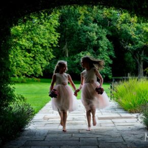 Photography of two young flower girls running and giggling through the pretty gardens at this Sopwell House wedding