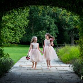 Two young flower girls dashing around the lush green gardens at Sopwell House