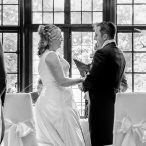 Photography of the indoor wedding civil ceremony in progress at the Bay Tree Hotel with a dramatic feature window framing the couple during their vows at their Burford venue