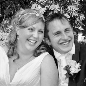 Black and white image of the smiling bride and groom posing for the camera in the hotel's gardens