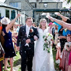 Photography of the bride and groom walking through the colourful sea of confetti after their ceremony at their Bay Tree Hotel wedding in Burford