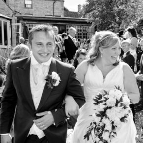 Photography of the smiling bride and groom walking through the confetti aisle with guests either side at their Bay Tree Hotel wedding in Burford