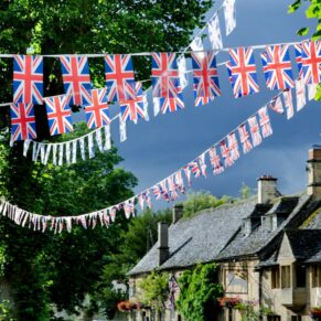 Photography of colourful union jack bunting zig zags between the roof tops in the street outside this Bay Tree Hotel wedding in Burford
