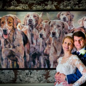Photography of the bride & groom as they pose for an atmospheric portrait beside a large oil painting inside the Bay Tree Hotel in Burford