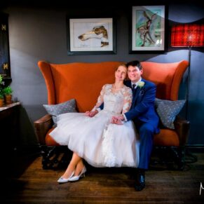 Photography of the newlyweds relaxing on an orange sofa in the bar area of the historic Bay Tree Hotel in Burford on their wedding day