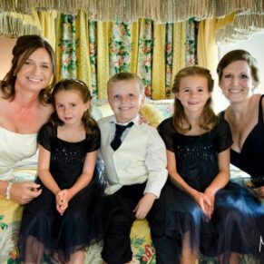 Photography of the bride with her wedding attendants snuggling up for a shot pre wedding ceremony whilst sat on the four poster bed at The Bay Tree Hotel in Burford