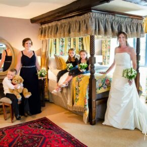 The bride and bridesmaids gather for a portrait next to the four poster bed in the bridal suite
