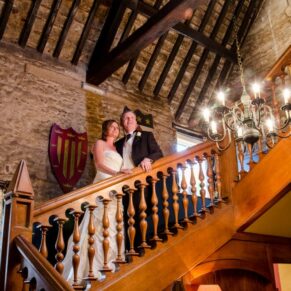 Photography of the bride and groom as they pose for the camera on the grand historic staircase at their Bay Tree Hotel wedding in Burford