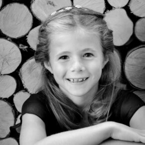 Smiling flower girl portrait with logs backdrop captured inside the Bay Tree Hotel