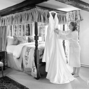 Photography of the wedding gown being tended to by the bride whilst it hangs from her four poster bed in the bridal suite at the Bay Tree Hotel in Burford