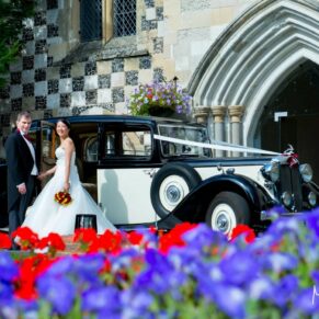 The newlyweds with their vintage wedding car at the front of Bisham Abbey and framed by gorgeous flower borders