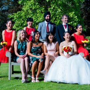 A small group of friends pose for a relaxed photo on a bench with the bride and groom at Bisham Abbey