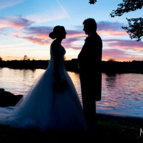 The sun setting on the atmospheric River Thames with the newlyweds in the foreground holding hands at their Bisham Abbey wedding