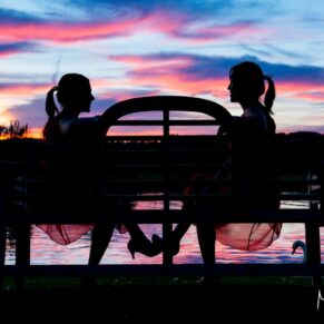 Wedding pose of the two bridesmaids sat on a bench with a stunning sunset and water reflections for our backdrop at Bisham Abbey
