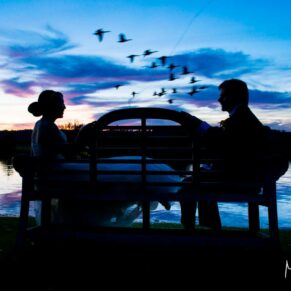 Striking sunset pose of the bride and groom with birds flying past along the River Thames at their Bisham Abbey summer wedding