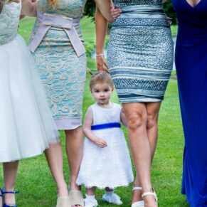 Cute shot of the flower girl hidden behind the ladies during the drinks reception