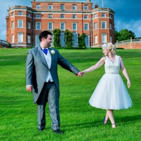 The smiling newlyweds taking a stroll through the famous estate with the main house behind them