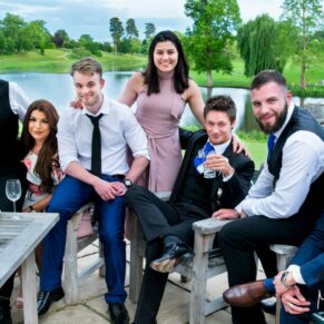 Photography of a relaxed wedding friends group pose on the terrace with the lake off in the distance at Brocket Hall in Hertfordshire