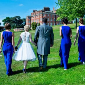 Photography of the wedding bridal party taking a stroll in the direction of the main house under perfect blue skies at Brocket Hall in Hertfordshire