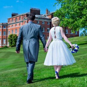 Photography of the newlyweds casually walking towards the manor house under perfect blue skies at their Brocket Hall wedding in Hertfordshire